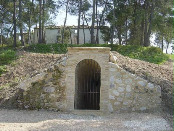 Entrada restaurada de un refugio antiaéreo excavado en una ladera, con arco de ladrillo y reja de hierro.