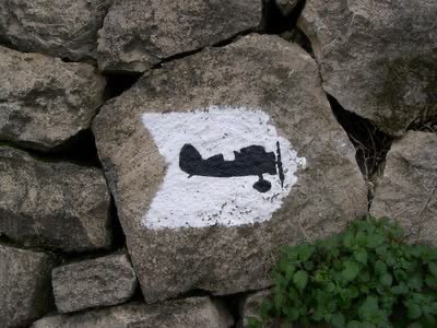 Piedra con la silueta de un avión de la época pintada en blanco y negro, señal que marca la ruta del aeródromo.